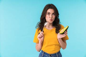 Serious woman holding avocado and spoon.
