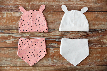 babyhood and clothing concept - baby hats with ears and bibs on wooden table