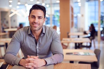 Portrait Of Businessman At Desk In Modern Office Work Space With Closed Laptop