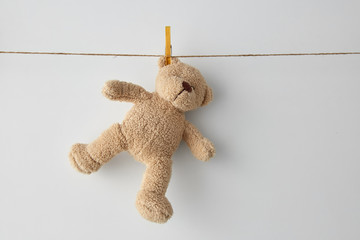 childhood and laundry concept - soft teddy bear toy hanging on clothesline on white background