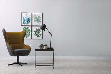 Stylish room interior with comfortable armchair and paintings of tropical leaves. Space for text