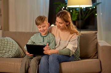 family, technology and people concept - happy mother and little son sitting on sofa and using tablet pc computer at home