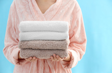 Woman holding stack of fresh clean towels on light blue background, closeup