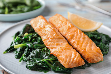 Tasty salmon with spinach and lemon on plate, closeup