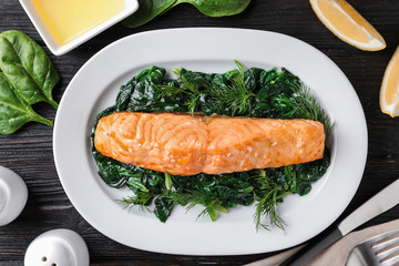 Tasty salmon with spinach on black wooden table, flat lay