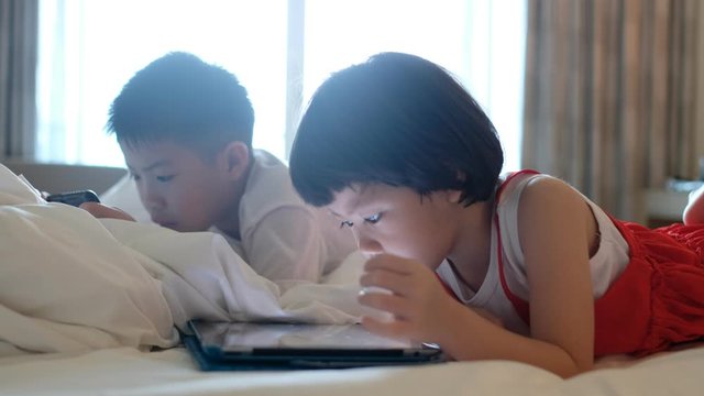 two chinese children addicted tablet, asian child watching tablet, kid use telephone together on their bed, play phone, kid addict smartphone