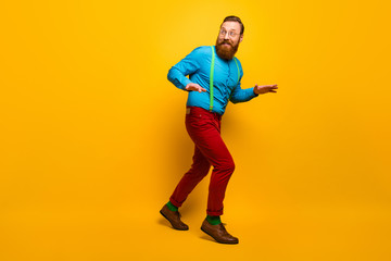 Fototapeta na wymiar Full length photo of attractive guy slow hush steps hiding girlfriend making surprise visit wear blue shirt green suspenders red pants socks footwear isolated yellow color background