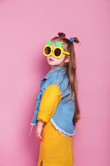 fashionable little girl in big pineapple sunglasses posing on pink background