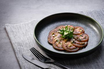 Sliced fresh kumato tomatoes with seasoning on grey background. Fresh vegetable vegetarian salad on round plate. Healthy vegan food. Copy space