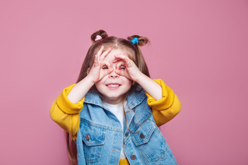 Funny little girl do funny double OK sign as glasses on pink background