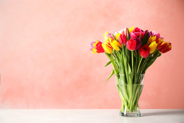Beautiful spring tulips in vase on table against light  pink background. Space for text