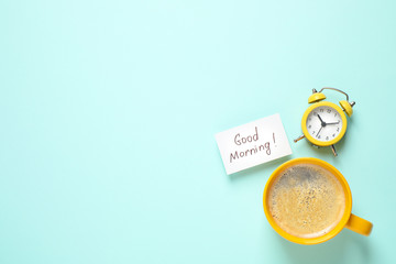 Message GOOD MORNING, alarm clock and coffee on light blue background, flat lay. Space for text