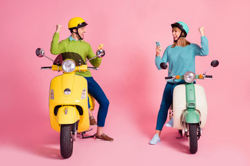 Full length photo of millennial lady guy two people sit vintage moped vacation short stop browsing telephone read sms raise fists wear casual jumper headgear isolated pink color background