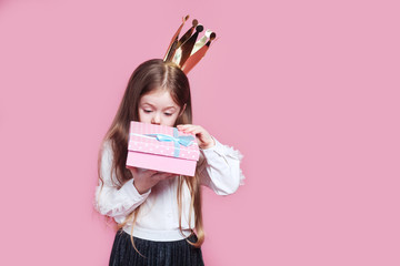 Happy little girl in crown and a white dress opening birthday present box