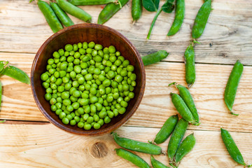 closeup green peas in brown dish, on wooden table.