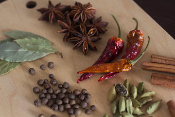 cardamom, black aroma pepper, star anis, dry hot red pepper and bay leaf on a wooden cutting board on a kitchen table