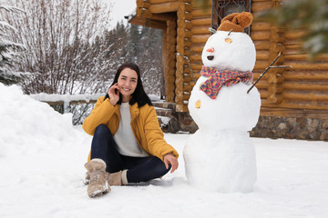 Young woman near funny snowman outdoors. Winter vacation