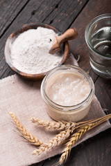 Fresh homemade bubbly sourdough starter, a fermented mixture of water and flour to use as leaven for bread baking, on wooden table