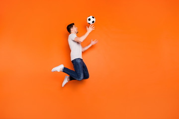 Fototapeta na wymiar Full size profile photo of funky guy jump high up catch football ball addicted fan goalkeeper wear striped t-shirt jeans sneakers isolated bright orange color background
