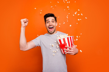 Photo of attractive crazy funky guy watch television humor show eat popcorn raise fist glad series beginning wear striped t-shirt isolated bright orange color background