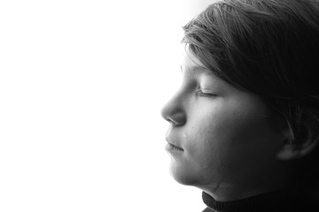 Black and white portrait of young sad boy crying with closed eyes. White background. Free space for...