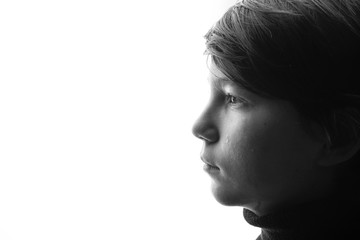 Black and white portrait of young sad boy crying with sad eyes. White background. Free space for text. Tear on cheek of unhappy teenager.