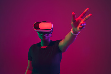 Pointing, touching. African-american young woman's portrait on purple background. Beautiful model in VR-headset. Concept of emotions, facial expression, sales, ad, inclusion, diversity. Copyspace.