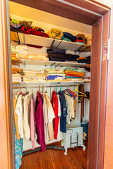 Storage room in the cottage with shelves and hangers, where different clothes hang and lie-t-shirts, shirts, pants, underwear