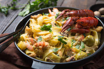 Fototapeta na wymiar Seafood fettuccine pasta with crayfishes, octopus shrims, on stone pan. Gourmet dish