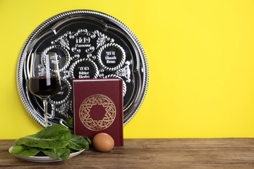 Symbolic Pesach (Passover Seder) items on wooden table against yellow background, space for text