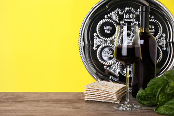 Symbolic Pesach (Passover Seder) items on wooden table against yellow background, space for text