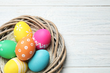 Decorative nest with Easter eggs on white wooden background, top view