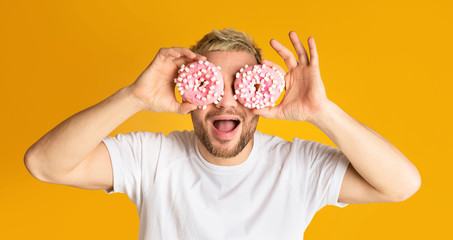 Guy have fun, holds donuts near eyes