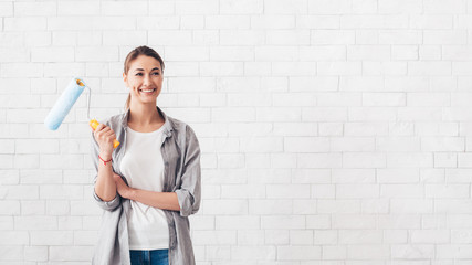 Young woman holding paint roller for renovation at home - Powered by Adobe