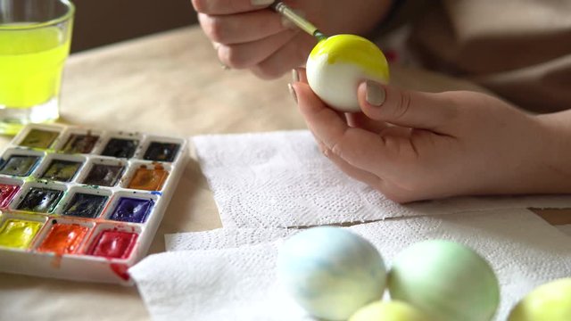 Female hands painting eggs with watercolors preparing for Easter celebration