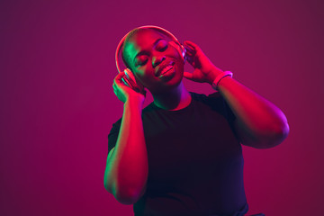 Listen to music. African-american young woman's portrait on purple background. Beautiful model in...