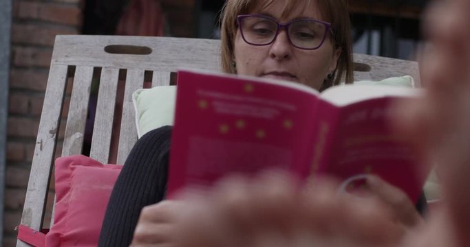 blond woman with glasses reading a book in the garden background the deck chair mid day confortable feets at front black magic cc