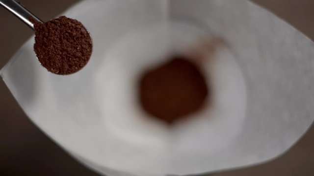 Scoop of coffee powder, coming from upper angle into the frame with blurred ground beans in the background. Slow motion.