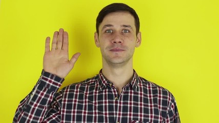 Close up portrait of a young attractive guy, he is smiling and waving goodbye to his friends. Portrait on a yellow background.