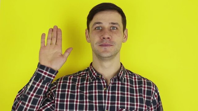 Close up portrait of a young attractive guy, he is smiling and waving goodbye to his friends. Portrait on a yellow background.