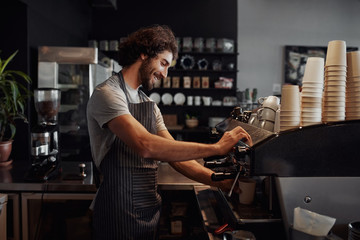 Smiling man with apron preparing coffee for customer in his small business - obrazy, fototapety, plakaty