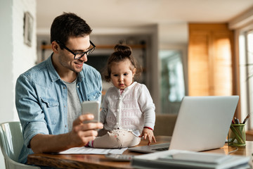 Happy father talking to his cute daughter while using smart phone at home.