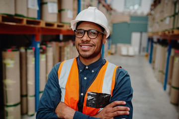 Portrait of handsome cheerful supervisor in warehouse standing with folded hands with material...