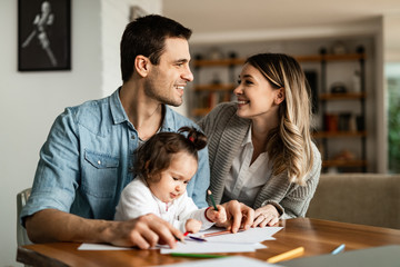 Happy parents talking while drawing with their small daughter at home.
