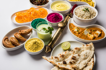 Happy Holy concept  showing Indian assorted lunch food like paneer butter masala, naan, jeera rice, black chana fry, jalebi, fujiyama, thandai and Farsan with holi colours and pichkari 