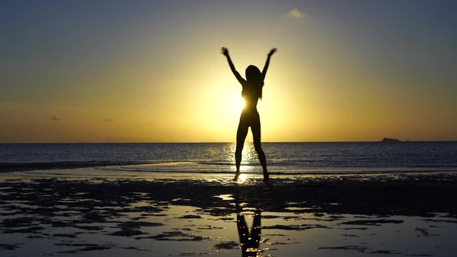 Happy young woman dancing on a tropical beach during sunset. Dance of caucasian girl near sea water