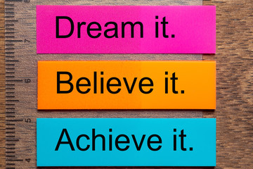 Three bookmark stickers with the words dream it, believe it, achieve it, on a dark natural wooden...