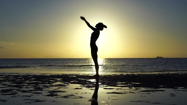 Silhouette of woman practicing at yoga pose on the tropical beach during sunset. Caucasian girl practicing yoga near sea water