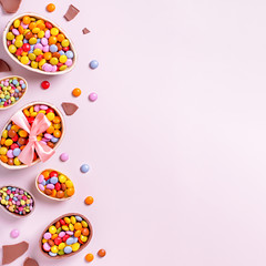 Chocolate Easter border with chocolate eggs and colorful candy sweets on pastel pink, copy space. Traditional Easter treats flat lay, holiday background