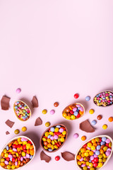 Chocolate Easter border with chocolate eggs and colorful candy sweets on pastel pink, copy space. Traditional Easter treats flat lay, holiday background